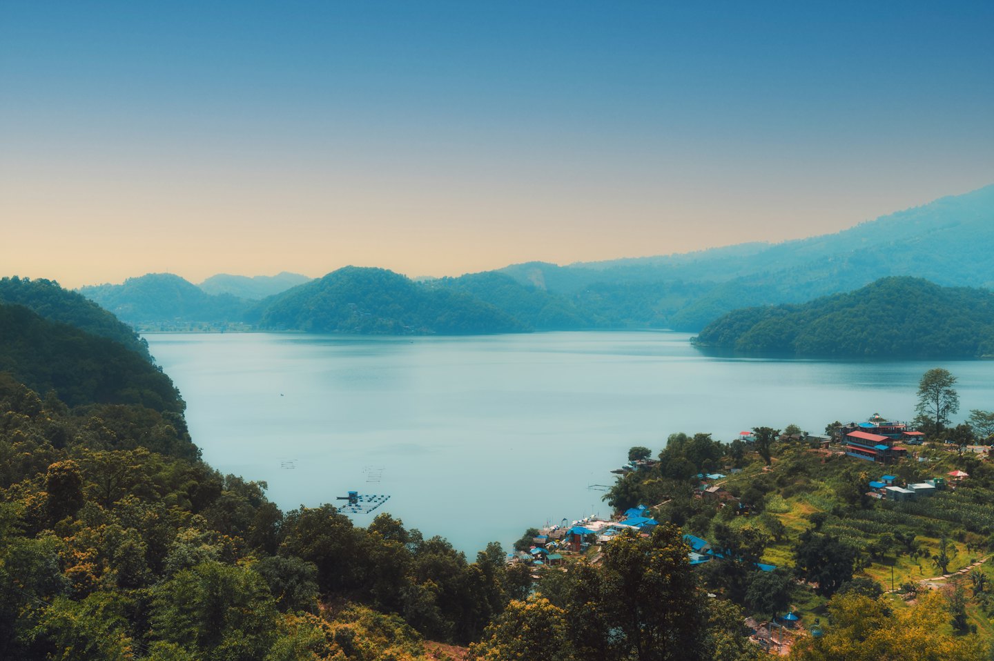 Lago con colline boscose e un villaggio sulla sua riva.