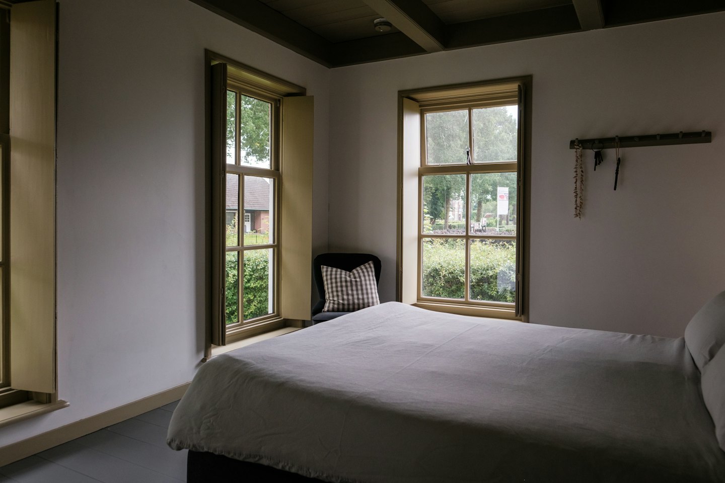 Camera da letto con soffitto a travi in legno e finestre con vista su alberi verdi.
