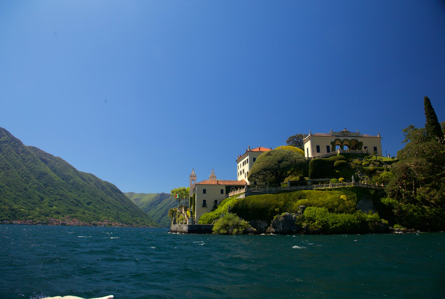Una grande villa su una collina verde vicino a un lago.