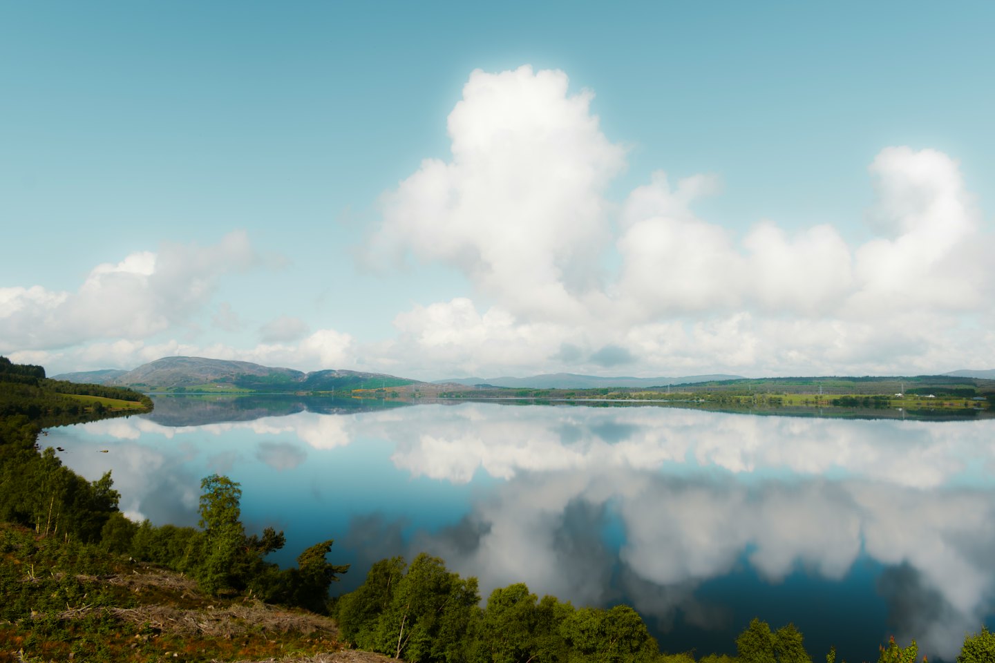 Acqua di lago riflettente circondata da colline verdi e terreno boscoso.